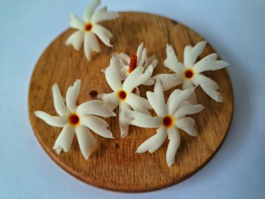 Servis tahtasındaki taze parijat çiçekleri. Çeşitli kullanımları var, hem tıbbi hem de kültürel. Ayurvedic tıpta ateş, öksürük ve soğuk algınlığını tedavi etmek için kullanılır. Çiçekler Hindu ayinlerinde ve tanrılara adak olarak da kullanılır.