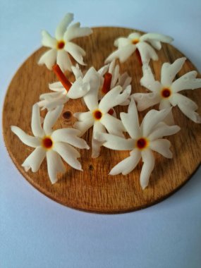 Servis tahtasındaki taze parijat çiçekleri. Çeşitli kullanımları var, hem tıbbi hem de kültürel. Ayurvedic tıpta ateş, öksürük ve soğuk algınlığını tedavi etmek için kullanılır. Çiçekler Hindu ayinlerinde ve tanrılara adak olarak da kullanılır.