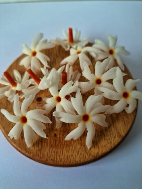 Servis tahtasındaki taze parijat çiçekleri. Çeşitli kullanımları var, hem tıbbi hem de kültürel. Ayurvedic tıpta ateş, öksürük ve soğuk algınlığını tedavi etmek için kullanılır. Çiçekler Hindu ayinlerinde ve tanrılara adak olarak da kullanılır.