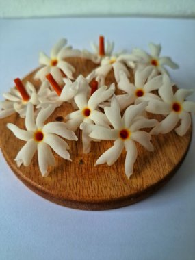 Servis tahtasındaki taze parijat çiçekleri. Çeşitli kullanımları var, hem tıbbi hem de kültürel. Ayurvedic tıpta ateş, öksürük ve soğuk algınlığını tedavi etmek için kullanılır. Çiçekler Hindu ayinlerinde ve tanrılara adak olarak da kullanılır.