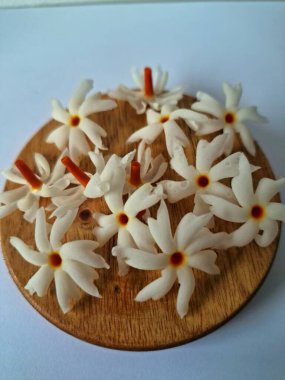 Servis tahtasındaki taze parijat çiçekleri. Çeşitli kullanımları var, hem tıbbi hem de kültürel. Ayurvedic tıpta ateş, öksürük ve soğuk algınlığını tedavi etmek için kullanılır. Çiçekler Hindu ayinlerinde ve tanrılara adak olarak da kullanılır.