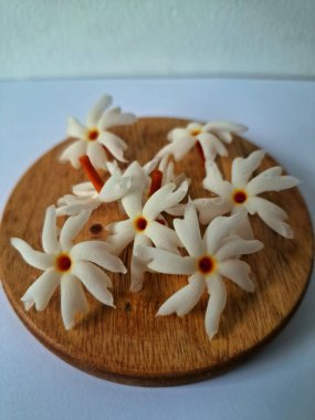 Servis tahtasındaki taze parijat çiçekleri. Çeşitli kullanımları var, hem tıbbi hem de kültürel. Ayurvedic tıpta ateş, öksürük ve soğuk algınlığını tedavi etmek için kullanılır. Çiçekler Hindu ayinlerinde ve tanrılara adak olarak da kullanılır.