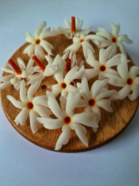 Servis tahtasındaki taze parijat çiçekleri. Çeşitli kullanımları var, hem tıbbi hem de kültürel. Ayurvedic tıpta ateş, öksürük ve soğuk algınlığını tedavi etmek için kullanılır. Çiçekler Hindu ayinlerinde ve tanrılara adak olarak da kullanılır.