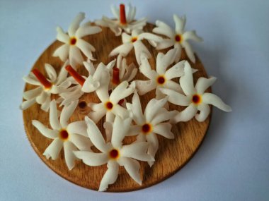 Servis tahtasındaki taze parijat çiçekleri. Çeşitli kullanımları var, hem tıbbi hem de kültürel. Ayurvedic tıpta ateş, öksürük ve soğuk algınlığını tedavi etmek için kullanılır. Çiçekler Hindu ayinlerinde ve tanrılara adak olarak da kullanılır.