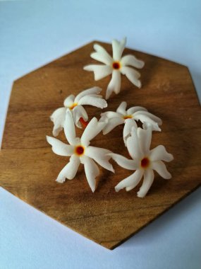 Servis tahtasındaki taze parijat çiçekleri. Çeşitli kullanımları var, hem tıbbi hem de kültürel. Ayurvedic tıpta ateş, öksürük ve soğuk algınlığını tedavi etmek için kullanılır. Çiçekler Hindu ayinlerinde ve tanrılara adak olarak da kullanılır.