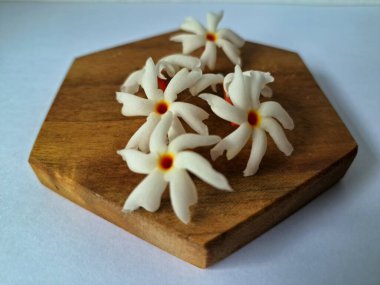 Servis tahtasındaki taze parijat çiçekleri. Çeşitli kullanımları var, hem tıbbi hem de kültürel. Ayurvedic tıpta ateş, öksürük ve soğuk algınlığını tedavi etmek için kullanılır. Çiçekler Hindu ayinlerinde ve tanrılara adak olarak da kullanılır.