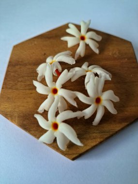 Servis tahtasındaki taze parijat çiçekleri. Çeşitli kullanımları var, hem tıbbi hem de kültürel. Ayurvedic tıpta ateş, öksürük ve soğuk algınlığını tedavi etmek için kullanılır. Çiçekler Hindu ayinlerinde ve tanrılara adak olarak da kullanılır.