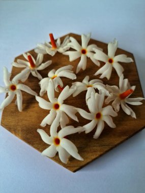 Servis tahtasındaki taze parijat çiçekleri. Çeşitli kullanımları var, hem tıbbi hem de kültürel. Ayurvedic tıpta ateş, öksürük ve soğuk algınlığını tedavi etmek için kullanılır. Çiçekler Hindu ayinlerinde ve tanrılara adak olarak da kullanılır.