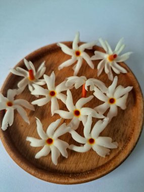 Servis tahtasındaki taze parijat çiçekleri. Çeşitli kullanımları var, hem tıbbi hem de kültürel. Ayurvedic tıpta ateş, öksürük ve soğuk algınlığını tedavi etmek için kullanılır. Çiçekler Hindu ayinlerinde ve tanrılara adak olarak da kullanılır.