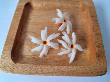 Tahta üzerinde taze parijat çiçekleri. Çeşitli kullanımları var, hem tıbbi hem de kültürel. Ayurvedic tıpta ateş, öksürük ve soğuk algınlığını tedavi etmek için kullanılır. Çiçekler Hindu ayinlerinde ve tanrılara adak olarak da kullanılır.