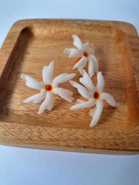 Tahta üzerinde taze parijat çiçekleri. Çeşitli kullanımları var, hem tıbbi hem de kültürel. Ayurvedic tıpta ateş, öksürük ve soğuk algınlığını tedavi etmek için kullanılır. Çiçekler Hindu ayinlerinde ve tanrılara adak olarak da kullanılır.