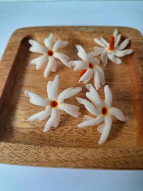 Tahta üzerinde taze parijat çiçekleri. Çeşitli kullanımları var, hem tıbbi hem de kültürel. Ayurvedic tıpta ateş, öksürük ve soğuk algınlığını tedavi etmek için kullanılır. Çiçekler Hindu ayinlerinde ve tanrılara adak olarak da kullanılır.