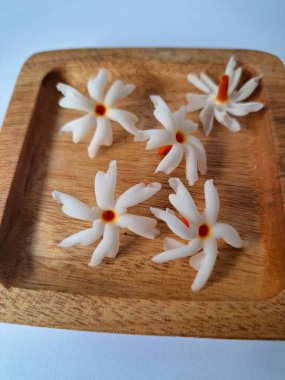 Tahta üzerinde taze parijat çiçekleri. Çeşitli kullanımları var, hem tıbbi hem de kültürel. Ayurvedic tıpta ateş, öksürük ve soğuk algınlığını tedavi etmek için kullanılır. Çiçekler Hindu ayinlerinde ve tanrılara adak olarak da kullanılır.