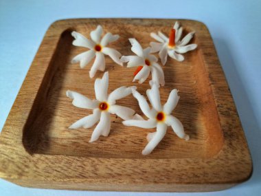 Tahta üzerinde taze parijat çiçekleri. Çeşitli kullanımları var, hem tıbbi hem de kültürel. Ayurvedic tıpta ateş, öksürük ve soğuk algınlığını tedavi etmek için kullanılır. Çiçekler Hindu ayinlerinde ve tanrılara adak olarak da kullanılır.