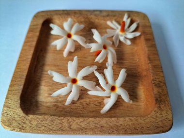 Tahta üzerinde taze parijat çiçekleri. Çeşitli kullanımları var, hem tıbbi hem de kültürel. Ayurvedic tıpta ateş, öksürük ve soğuk algınlığını tedavi etmek için kullanılır. Çiçekler Hindu ayinlerinde ve tanrılara adak olarak da kullanılır.