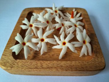 Tahta üzerinde taze parijat çiçekleri. Çeşitli kullanımları var, hem tıbbi hem de kültürel. Ayurvedic tıpta ateş, öksürük ve soğuk algınlığını tedavi etmek için kullanılır. Çiçekler Hindu ayinlerinde ve tanrılara adak olarak da kullanılır.