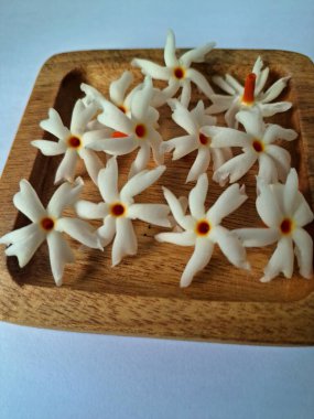 Tahta üzerinde taze parijat çiçekleri. Çeşitli kullanımları var, hem tıbbi hem de kültürel. Ayurvedic tıpta ateş, öksürük ve soğuk algınlığını tedavi etmek için kullanılır. Çiçekler Hindu ayinlerinde ve tanrılara adak olarak da kullanılır.