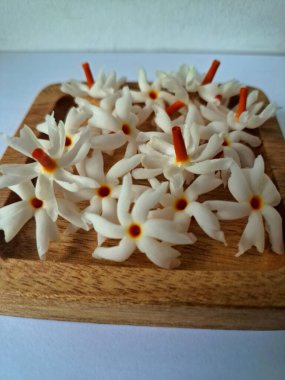 Tahta üzerinde taze parijat çiçekleri. Çeşitli kullanımları var, hem tıbbi hem de kültürel. Ayurvedic tıpta ateş, öksürük ve soğuk algınlığını tedavi etmek için kullanılır. Çiçekler Hindu ayinlerinde ve tanrılara adak olarak da kullanılır.