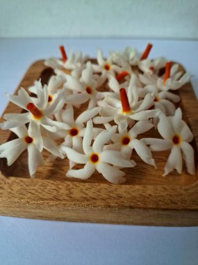 Tahta üzerinde taze parijat çiçekleri. Çeşitli kullanımları var, hem tıbbi hem de kültürel. Ayurvedic tıpta ateş, öksürük ve soğuk algınlığını tedavi etmek için kullanılır. Çiçekler Hindu ayinlerinde ve tanrılara adak olarak da kullanılır.