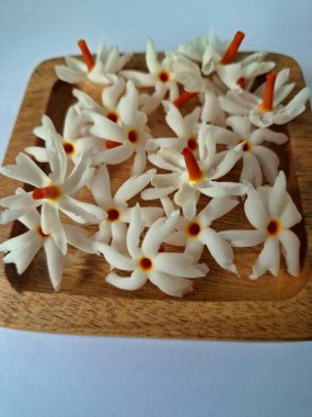 Tahta üzerinde taze parijat çiçekleri. Çeşitli kullanımları var, hem tıbbi hem de kültürel. Ayurvedic tıpta ateş, öksürük ve soğuk algınlığını tedavi etmek için kullanılır. Çiçekler Hindu ayinlerinde ve tanrılara adak olarak da kullanılır.