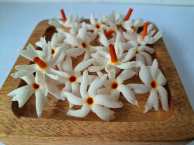 Tahta üzerinde taze parijat çiçekleri. Çeşitli kullanımları var, hem tıbbi hem de kültürel. Ayurvedic tıpta ateş, öksürük ve soğuk algınlığını tedavi etmek için kullanılır. Çiçekler Hindu ayinlerinde ve tanrılara adak olarak da kullanılır.