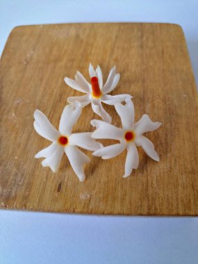 Tahta üzerinde taze parijat çiçekleri. Çeşitli kullanımları var, hem tıbbi hem de kültürel. Ayurvedic tıpta ateş, öksürük ve soğuk algınlığını tedavi etmek için kullanılır. Çiçekler Hindu ayinlerinde ve tanrılara adak olarak da kullanılır.