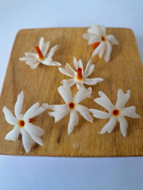 Tahta üzerinde taze parijat çiçekleri. Çeşitli kullanımları var, hem tıbbi hem de kültürel. Ayurvedic tıpta ateş, öksürük ve soğuk algınlığını tedavi etmek için kullanılır. Çiçekler Hindu ayinlerinde ve tanrılara adak olarak da kullanılır.