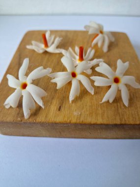 Tahta üzerinde taze parijat çiçekleri. Çeşitli kullanımları var, hem tıbbi hem de kültürel. Ayurvedic tıpta ateş, öksürük ve soğuk algınlığını tedavi etmek için kullanılır. Çiçekler Hindu ayinlerinde ve tanrılara adak olarak da kullanılır.