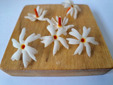 Tahta üzerinde taze parijat çiçekleri. Çeşitli kullanımları var, hem tıbbi hem de kültürel. Ayurvedic tıpta ateş, öksürük ve soğuk algınlığını tedavi etmek için kullanılır. Çiçekler Hindu ayinlerinde ve tanrılara adak olarak da kullanılır.