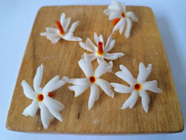 Tahta üzerinde taze parijat çiçekleri. Çeşitli kullanımları var, hem tıbbi hem de kültürel. Ayurvedic tıpta ateş, öksürük ve soğuk algınlığını tedavi etmek için kullanılır. Çiçekler Hindu ayinlerinde ve tanrılara adak olarak da kullanılır.