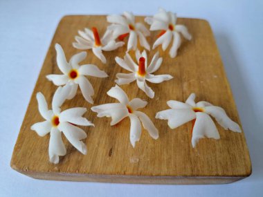 Tahta üzerinde taze parijat çiçekleri. Çeşitli kullanımları var, hem tıbbi hem de kültürel. Ayurvedic tıpta ateş, öksürük ve soğuk algınlığını tedavi etmek için kullanılır. Çiçekler Hindu ayinlerinde ve tanrılara adak olarak da kullanılır.