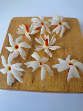 Tahta üzerinde taze parijat çiçekleri. Çeşitli kullanımları var, hem tıbbi hem de kültürel. Ayurvedic tıpta ateş, öksürük ve soğuk algınlığını tedavi etmek için kullanılır. Çiçekler Hindu ayinlerinde ve tanrılara adak olarak da kullanılır.