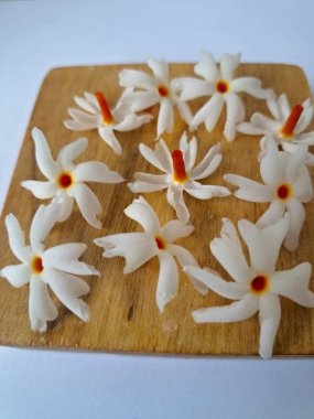 Tahta üzerinde taze parijat çiçekleri. Çeşitli kullanımları var, hem tıbbi hem de kültürel. Ayurvedic tıpta ateş, öksürük ve soğuk algınlığını tedavi etmek için kullanılır. Çiçekler Hindu ayinlerinde ve tanrılara adak olarak da kullanılır.