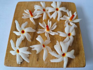 Tahta üzerinde taze parijat çiçekleri. Çeşitli kullanımları var, hem tıbbi hem de kültürel. Ayurvedic tıpta ateş, öksürük ve soğuk algınlığını tedavi etmek için kullanılır. Çiçekler Hindu ayinlerinde ve tanrılara adak olarak da kullanılır.