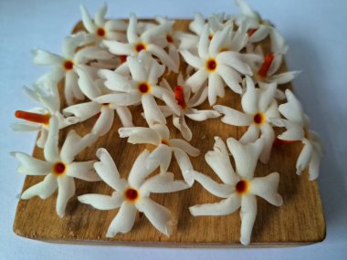 Tahta üzerinde taze parijat çiçekleri. Çeşitli kullanımları var, hem tıbbi hem de kültürel. Ayurvedic tıpta ateş, öksürük ve soğuk algınlığını tedavi etmek için kullanılır. Çiçekler Hindu ayinlerinde ve tanrılara adak olarak da kullanılır.