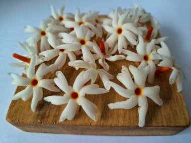 Tahta üzerinde taze parijat çiçekleri. Çeşitli kullanımları var, hem tıbbi hem de kültürel. Ayurvedic tıpta ateş, öksürük ve soğuk algınlığını tedavi etmek için kullanılır. Çiçekler Hindu ayinlerinde ve tanrılara adak olarak da kullanılır.