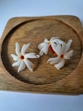 Tahta üzerinde taze parijat çiçekleri. Çeşitli kullanımları var, hem tıbbi hem de kültürel. Ayurvedic tıpta ateş, öksürük ve soğuk algınlığını tedavi etmek için kullanılır. Çiçekler Hindu ayinlerinde ve tanrılara adak olarak da kullanılır.