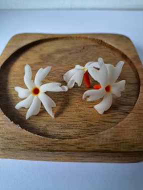 Tahta üzerinde taze parijat çiçekleri. Çeşitli kullanımları var, hem tıbbi hem de kültürel. Ayurvedic tıpta ateş, öksürük ve soğuk algınlığını tedavi etmek için kullanılır. Çiçekler Hindu ayinlerinde ve tanrılara adak olarak da kullanılır.