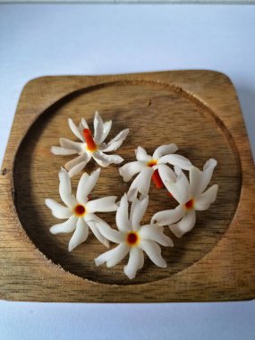 Tahta üzerinde taze parijat çiçekleri. Çeşitli kullanımları var, hem tıbbi hem de kültürel. Ayurvedic tıpta ateş, öksürük ve soğuk algınlığını tedavi etmek için kullanılır. Çiçekler Hindu ayinlerinde ve tanrılara adak olarak da kullanılır.