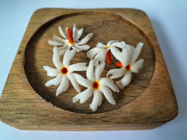 Tahta üzerinde taze parijat çiçekleri. Çeşitli kullanımları var, hem tıbbi hem de kültürel. Ayurvedic tıpta ateş, öksürük ve soğuk algınlığını tedavi etmek için kullanılır. Çiçekler Hindu ayinlerinde ve tanrılara adak olarak da kullanılır.