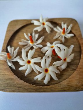 Tahta üzerinde taze parijat çiçekleri. Çeşitli kullanımları var, hem tıbbi hem de kültürel. Ayurvedic tıpta ateş, öksürük ve soğuk algınlığını tedavi etmek için kullanılır. Çiçekler Hindu ayinlerinde ve tanrılara adak olarak da kullanılır.