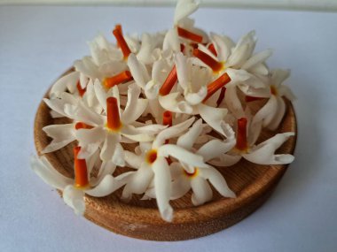 Tahta üzerinde taze parijat çiçekleri. Çeşitli kullanımları var, hem tıbbi hem de kültürel. Ayurvedic tıpta ateş, öksürük ve soğuk algınlığını tedavi etmek için kullanılır. Çiçekler Hindu ayinlerinde ve tanrılara adak olarak da kullanılır.