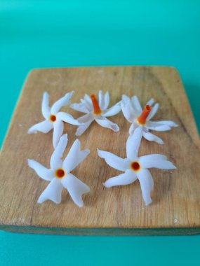 Servis tahtasındaki taze parijat çiçekleri. Çeşitli kullanımları var, hem tıbbi hem de kültürel. Ayurvedic tıpta ateş, öksürük ve soğuk algınlığını tedavi etmek için kullanılır. Çiçekler Hindu ayinlerinde ve tanrılara adak olarak da kullanılır.