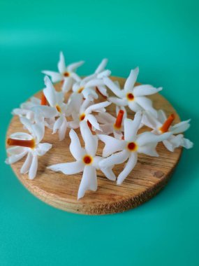 Servis tahtasındaki taze parijat çiçekleri. Çeşitli kullanımları var, hem tıbbi hem de kültürel. Ayurvedic tıpta ateş, öksürük ve soğuk algınlığını tedavi etmek için kullanılır. Çiçekler Hindu ayinlerinde ve tanrılara adak olarak da kullanılır.