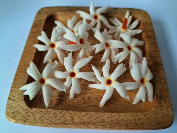 Tahta üzerinde taze parijat çiçekleri. Çeşitli kullanımları var, hem tıbbi hem de kültürel. Ayurvedic tıpta ateş, öksürük ve soğuk algınlığını tedavi etmek için kullanılır. Çiçekler Hindu ayinlerinde ve tanrılara adak olarak da kullanılır.