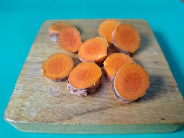 Servis tahtasında taze zerdeçal yumrusu dilimleri. Bu baharat Asya mutfağında yaygın olarak kullanılır, özellikle köri gibi yemeklerde tat ve renk için. Zerdeçal ayrıca aktif bileşik curkiminle birlikte tıbbi özelliklere de sahiptir.