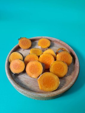 Servis tahtasında taze zerdeçal yumrusu dilimleri. Zerdeçal birçok sağlık yararına sahip bir bitkisel bitkidir. Zerdeçal sıklıkla geleneksel tıpta ve yemek pişirmede bir tat ve doğal renklendirme olarak kullanılır.