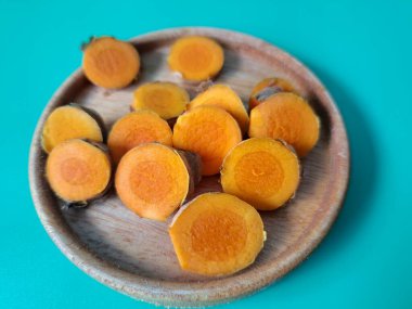 Servis tahtasında taze zerdeçal yumrusu dilimleri. Bu baharat Asya mutfağında yaygın olarak kullanılır, özellikle köri gibi yemeklerde tat ve renk için. Zerdeçal ayrıca aktif bileşik curkiminle birlikte tıbbi özelliklere de sahiptir.