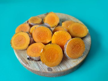 Servis tahtasında taze zerdeçal yumrusu dilimleri. Bu baharat Asya mutfağında yaygın olarak kullanılır, özellikle köri gibi yemeklerde tat ve renk için. Zerdeçal ayrıca aktif bileşik curkiminle birlikte tıbbi özelliklere de sahiptir.