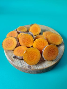 Servis tahtasında taze zerdeçal yumrusu dilimleri. Zerdeçal birçok sağlık yararına sahip bir bitkisel bitkidir. Zerdeçal sıklıkla geleneksel tıpta ve yemek pişirmede bir tat ve doğal renklendirme olarak kullanılır.